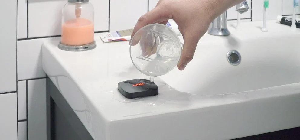 LeaksProtect Wassersensor auf einer Waschtischkante, in der Nähe wird Wasser verschüttet